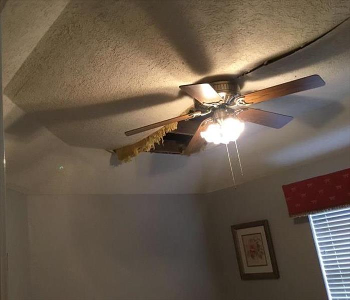 Bedroom ceiling caving in from water damage. Ceiling fan light is on. 